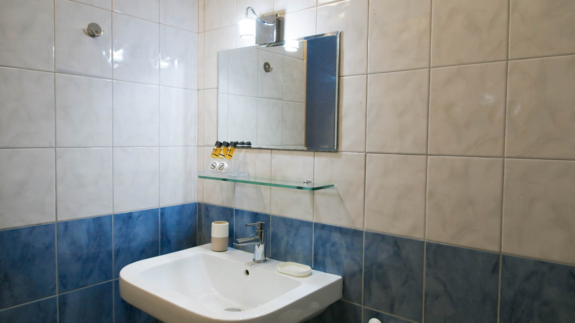 A sink and a mirror, with white and blue bathroom tiles behind.